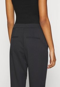 Mörkgrå skräddarsydda byxor med en jämn textur, med en platt midja och två bakfickor, synliga sömsdetaljer.