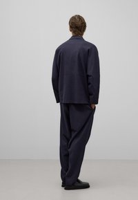 Chaqueta y pantalones sueltos de color azul oscuro hechos de tela texturizada. La chaqueta tiene un cuello mandarín; los pantalones cuentan con bolsillos laterales.