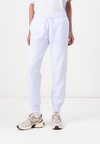 Light blue sweatpants made of soft fabric, featuring an elastic waistband with drawstring, cuffed ankles, and a subtle logo detail on the thigh.