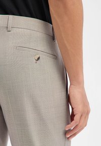 Hellgraue, maßgeschneiderte Hosen aus strukturiertem Stoff, mit einer Gesäßtasche mit Knopfverschluss und kontrastierenden Ziernähten.