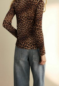 Camiseta de manga larga con estampado de leopardo hecha de tela elástica, combinada con vaqueros de tiro alto azul claro que tienen bolsillos traseros y un corte relajado.