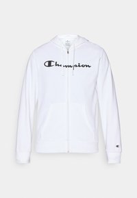 Hvit zip-up hettegenser laget av myk stoff, med en svart "Champion" logo på brystet, kengurulommer og ribbede mansjetter.