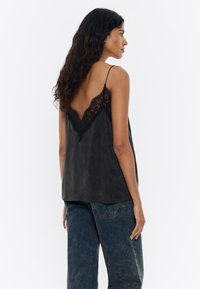 Camiseta de satén negro con encaje en el escote en V, con tirantes finos y un corte relajado, combinada con pantalones vaqueros de cintura alta.