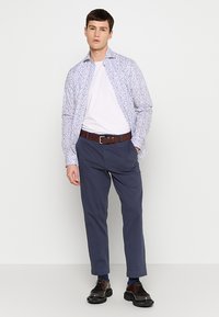Herenoutfit met een wit T-shirt, een blauw met patroon lange mouw overhemd, donkerblauwe broek en zwarte schoenen met een stevige zool.