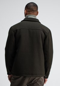 Dark green wool jacket with a structured collar and buttoned cuffs, featuring a smooth texture and classic cut for warmth. Back view.