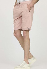 Shorts roses clairs à coupe droite, dotés de poches latérales, d'ourlets retroussés et de détails en tissu contrasté aux poignets. Portés avec des baskets blanches.