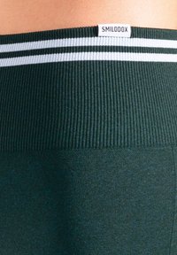 Mörkgrön träningsmidjeband med ribbad textur, med två vita ränder och en etikett med varumärkesnamnet "SMILODOX".