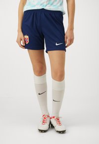Marinblå fotbollsshorts med en Norge-emblem, tillsammans med vita knähöga strumpor med svarta Nike-logotyper, och vita fotbollsskor med röda accenter.