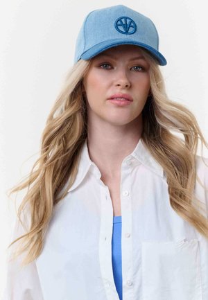 Young woman with long blonde hair wears a light blue baseball cap, white buttoned shirt, and blue top, facing forward with neutral expression.