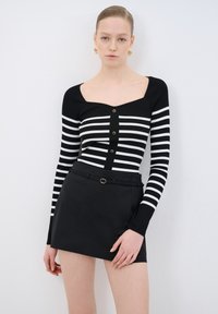 Maglione a righe bianco e nero con maniche lunghe, texture a coste, scollatura quadrata e cinque bottoni dorati. Abbinato a una mini gonna nera.