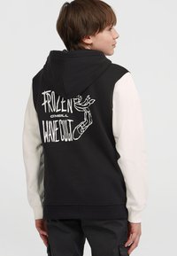 Czarny i kremowy hoodie z białym nadrukiem na plecach, na którym widnieje napis "FROZEN WAVE CUT." Posiada sznurek do regulacji kaptura oraz ściągacze na rękawach.