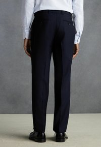 Pantalon de costume navy à coupe ajustée, doté de poches arrière avec boutons, en tissu lisse, associé à une chemise rayée bleu clair.