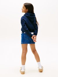 Felpa cropped blu navy con cappuccio, abbinata a una minigonna di jeans. Calze bianche e scarpe da ginnastica beige completano l'outfit.