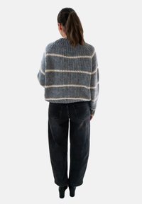 Grijze gebreide trui met witte strepen, cropped ontwerp en losse pasvorm, gecombineerd met zwarte wijde jeans. Zachte textuur, casual stijl.