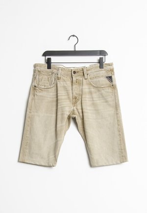 Beige Jeansshorts an einem schwarzen Bügel, mit Taschen vorne, Gürtelschlaufen und Knopfverschluss.