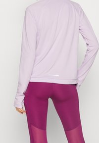 Maglia viola chiaro a maniche lunghe con scollatura rotonda e texture morbida, abbinata a leggings rosa scuro con pannelli in rete sui lati.