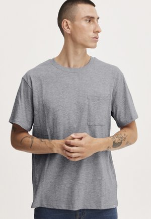 Gray cotton t-shirt with crew neck, short sleeves, and a chest pocket. Features a smooth texture and loose fit, worn with hands clasped.
