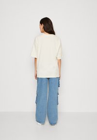 Krämfärgad oversized t-shirt som matchas med ljusblå vida cargo-jeans med sidofickor och fransade detaljer.