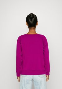 Sweat-shirt fuchsia avec un col rond et des manches raglan, doté d'un tissu texturé et de poignets côtelés, associé à un denim bleu clair.