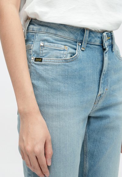 Jeans de ganga azul claro com cintura alta, cinco bolsos e uma pequena etiqueta da marca nas costas. Textura suave com um corte clássico.