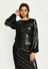 Zwarte pailletten top met lange, geblafde mouwen en een ronde halslijn, met een gladde textuur en glanzende afwerking. Draagt een bijpassende paillettenrok.