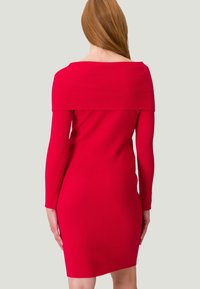 Robe rouge côtelée avec des manches longues et un design dénudé d'épaules. Coupe moulante, longueur mi-cuisse, texture lisse et détails minimes.
