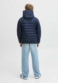 Mörkblå puffjacka med huva, med horisontellt kviltat mönster. Kombinerad med ljusblå vida jeans och blå sneakers.