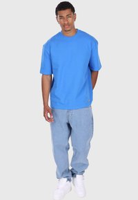 Blå bomull T-skjorte med avslappet passform, korte ermer, rund hals, parret med lys blå denimjeans og hvite joggesko.