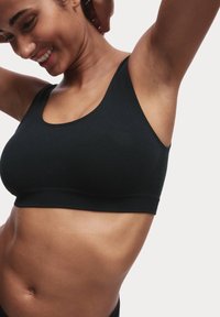 Sostenedor deportivo negro hecho de un tejido suave y elástico, con escote redondeado y tirantes anchos, diseñado para ofrecer comodidad y soporte sin acolchado.