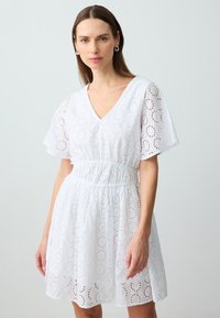 Weisses Kleid aus Lochstickerei mit V-Ausschnitt, kurzen, flatternden Ärmeln, elastischem Bund und kreisförmigen Ausschnitten throughout.