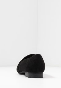 Chaussure en daim noir avec un petit talon. Caractérisée par un bout arrondi et une texture lisse. Design minimaliste sans motifs ni ornements visibles.