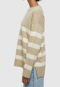 Pull beige et blanc à rayures avec col et poignets côtelés. Fentes latérales et coupe décontractée. Matière tricot douce.