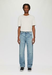 T-shirt en coton gris clair à manches courtes, associé à un jean déchiré taille haute bleu clair et des baskets noires à semelles blanches.