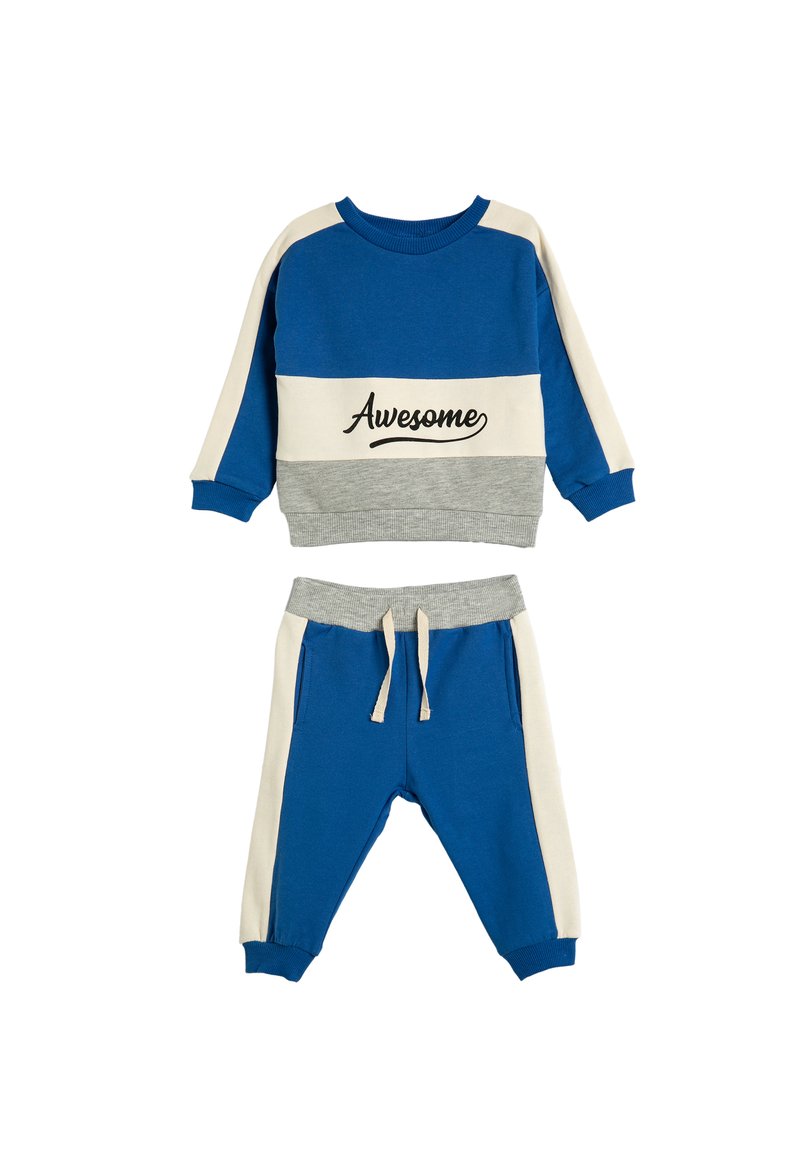 Twee-delig kinderoutfit in blauw, crème en grijs. De top heeft lange mouwen met de tekst "Awesome", en de broek heeft een elastische tailleband.