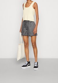 Haut en tricot crème avec des bords festonnés, associé à un short gris foncé avec une ceinture à nouer et une finition texturée, ainsi qu'à des baskets montantes noires.