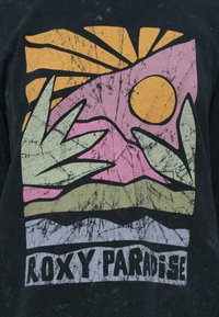 Svart t-skjorte med abstrakt design som har en oransje sol, rosa fjell, grønne blader og grå bunnstripe. Teksten sier "ROXY PARADISE."