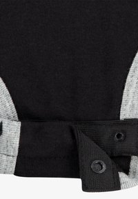 Čierna a sivá pletená látka s rebrovanou textúrou, opatrená cvokmi na leme. Dizajn obsahuje kontrastné farebné akcenty.