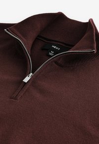 Bordeauxfarbener Pullover mit Reißverschlusskragen, aus weichem Strickstoff. Verfügt über einen silbernen Reißverschluss und Rippenstruktur am Kragen. Markenlabel sichtbar.