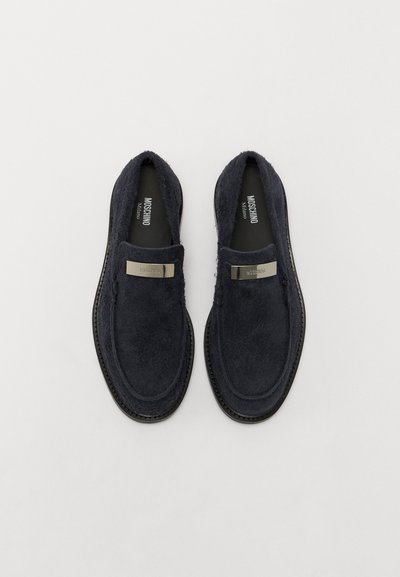 Sötétkék, slip-on stílusú cipők texturált felsőrésszel, fém márkázott táblával és gumitalppal. Sima felület, látható varrási részletekkel.