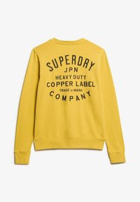 Żółta bluza z teksturowanym wykończeniem, z dużym czarnym nadrukiem graficznym z tyłu. Okrągły dekolt i długie rękawy. Casualowy design.