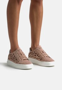 Sneaker rosa in suede con design perforato, dettagli testurizzati e suole in gomma bianca. Lacci e marchio visibili sulla linguetta.