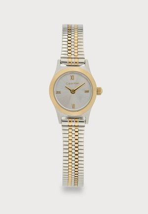 Silberne und goldene Calvin Klein Armbanduhr mit rundem Zifferblatt, römischen Zahlen bei 12, 3, 6, 9 und zweifarbigem Metallgliederarmband.