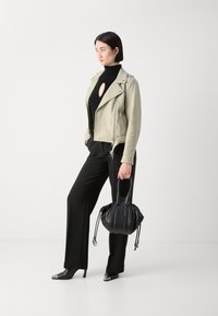 Jachetă biker din piele verde deschis, cu detalii argintii, purtată peste un pulover negru cu guler înalt. Asortată cu pantaloni negri și pantofi cu vârf ascuțit, ținând o geantă neagră.