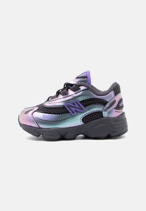 Sneaker chunky con tomaia iridescente viola e verde acqua, dettagli in mesh nero, logo "N" viola e suola spessa nera, vista laterale.