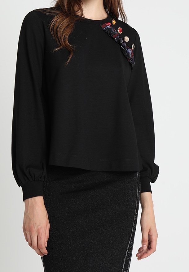 Svart långärmad topp med en avslappnad passform, med en texturerad tyg och en knäppning av färgglada knappar och mönstrat tyg längs axeln.