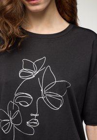 T-shirt nera a maniche corte con disegno a linea bianca di un volto e design di farfalle. Tessuto morbido, scollatura rotonda, vestibilità casual.