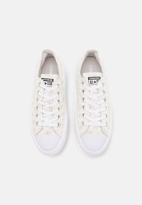 Vita canvas-sneakers med blommönster, gummitå och vita snören. Har "Converse All Star"-logotyp på tungan.