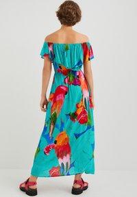 Robe maxi off-the-shoulder en tissu turquoise, ornée de motifs floraux vibrants et de perroquets. Accentuée de manches volantes et d'une taille cintrée.