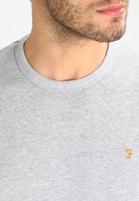 Sudadera gris de algodón mezclado con cuello redondo, que presenta un cuello acanalado y un pequeño logo dorado bordado en el pecho.