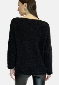 Maglione nero, morbido e lavorato a maglia con scollatura ampia e maniche lunghe, caratterizzato da una vestibilità comoda e tessuto testurizzato. Indossato con pantaloni neri eleganti.